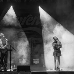 Das schwarz-weiß Bild zeigt zwei Künstler, links einen Mann am Keyboard und rechts eine Frau, als Sängerin am Mikrofon.