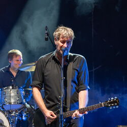 Sänger der Band an Gitarre und Mikrofon, im Hintergrund der Schlagzeuger.