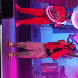 Die Musiker der Band im Einsatz bei lila Licht. Links ein Mann mit Sousaphon und rechts eine singendePerson die den linken Arm nach oben streckt.