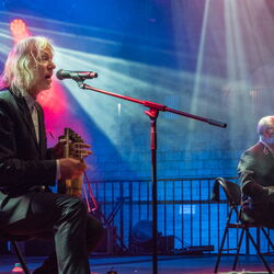 Zwei Musiker die auf Stühlen sitzen, ihr Instrument spielen und dazu singen.